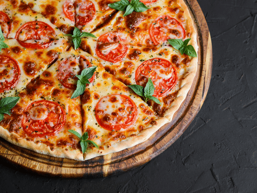A freshly baked pizza topped with cheese, tomatoes, and basil, placed on a wooden board with a dark backdrop