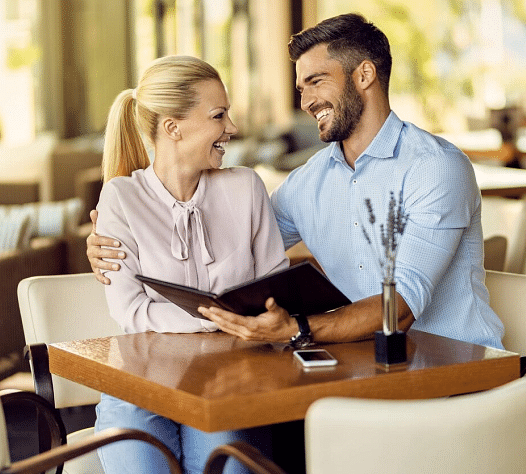 Two people looking at each other and smiling, the man with a menu card on his hand.