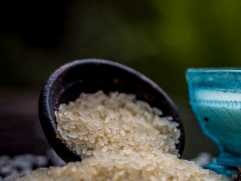 Uncooked white rice spilling from a dark wooden scoop beside a blue glass bowl