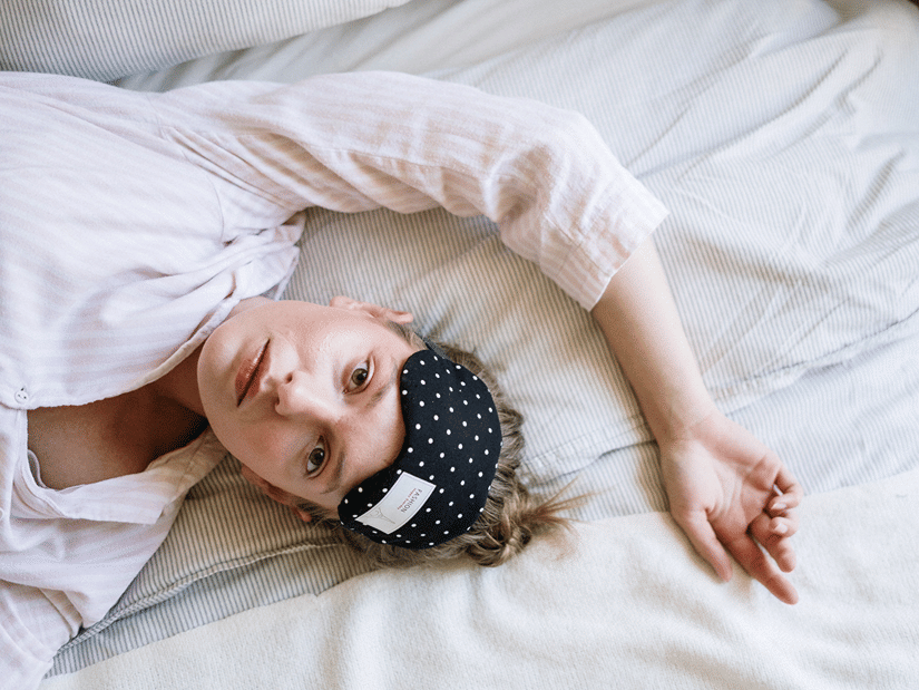 A woman lying in bed with a polka-dot sleep mask pushed up on her forehead