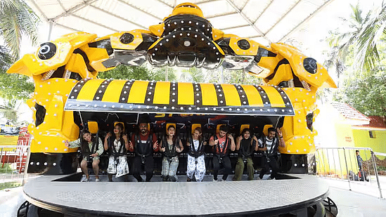 A group of people seated on a large yellow and black thrill ride, possibly a spinning or swinging attraction - Black Thunder Water Theme Park