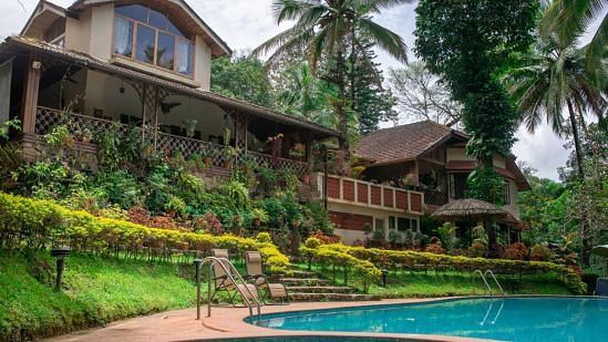 Buildings nestled amongst lush greenery beside a swimming pool in a tropical setting - BluSalzz Collection - Tranquil Resort, Wayanad
