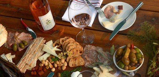 A rustic charcuterie board with assorted cheeses, crackers, olives, and wine on a wooden table.