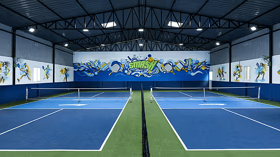 Wide-view of the indoor Pickleball court at Jenneys Residency with two courts side-by-side, ventilation and overhead lighting.