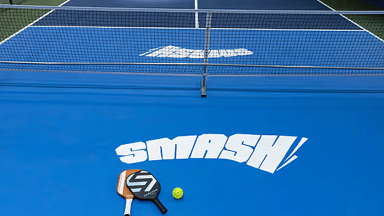 Close-up view of the indoor pickleball court at Jenneys Residency in Coimbatore with the text 'SMASH!' , a paddle and a ball.