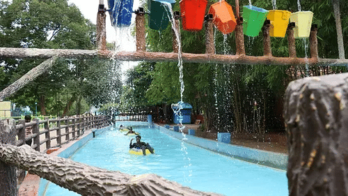 People relaxing in a lazy river with colorful flags overhead and lush greenery around - Black Thunder Water Theme Park