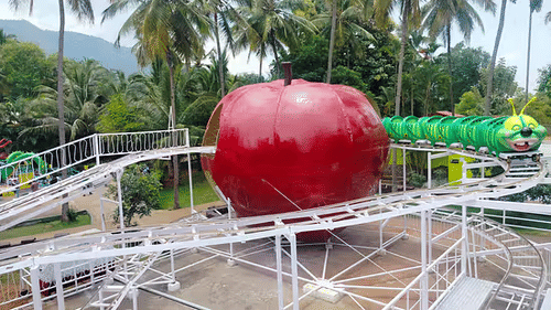 Apple-shaped roller coaster ride track at Black Thunder theme park nestled among tropical trees