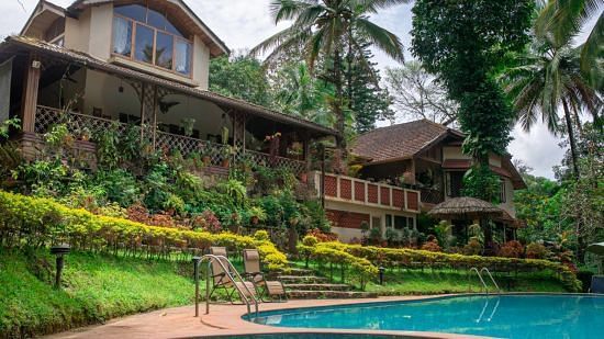 Buildings nestled amongst lush greenery beside a swimming pool in a tropical setting - BluSalzz Collection - Tranquil Resort, Wayanad