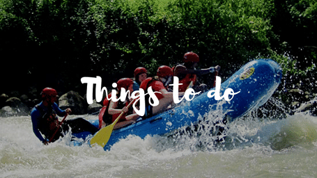 Group in helmets and life jackets white-water rafting through rapids, with a Things to do text