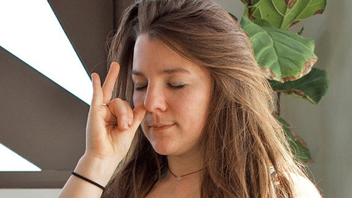 A person with long brown hair has closed eyes, with their right hand in a mudra, touching thumb and index finger at YO1 Longevity & Health Resorts