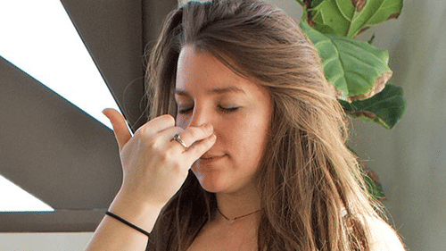 A person with long brown hair closes their eyes, using their right hand to pinch their nose, possibly for alternate nostril breathing at YO1 Longevity & Health Resorts