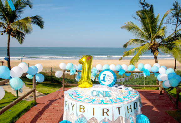 a 1st birthday cake kept outside on a table with balloons around - Caravela Beach Resort Goa