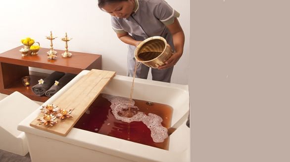 A tray with items and a person lying in a tub, indoor setting - Shreyas Retreat