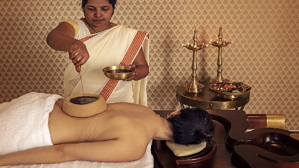 A therapist applying warm herbal oil to a client's back using traditional Ayurvedic techniques - Shreyas Retreat