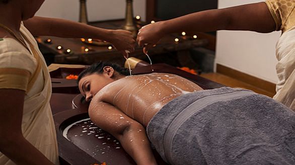 A therapist pouring warm herbal oil on a client’s back during an Ayurvedic treatment - Shreyas Retreat