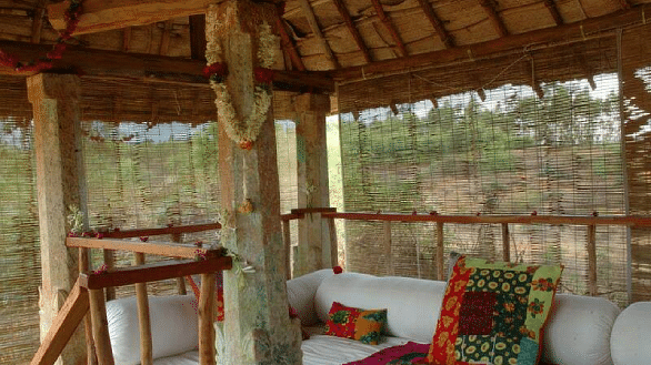 A covered outdoor patio with seating and a wooden railing, natural light - Shreyas Retreat