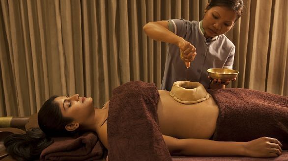 A therapist pouring liquid on a client's stomach during an Ayurvedic treatment - Shreyas Retreat