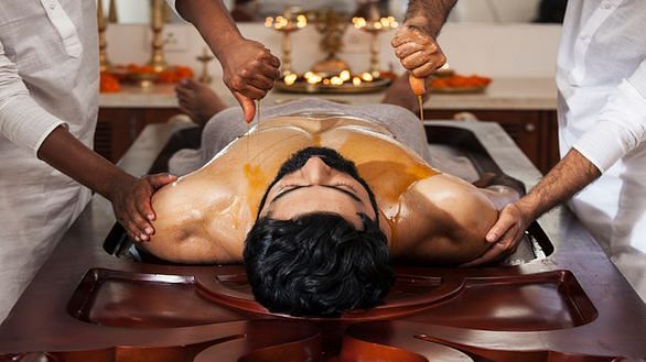 A person receiving a massage on a wooden table, with hands applying treatment - Shreyas Retreat
