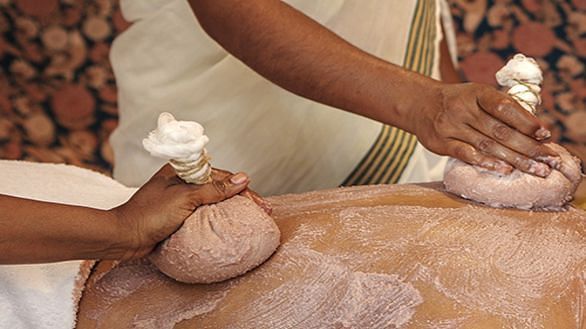 A close-up of hands applying an Ayurvedic herbal scrub to a client's body - Shreyas Retreat