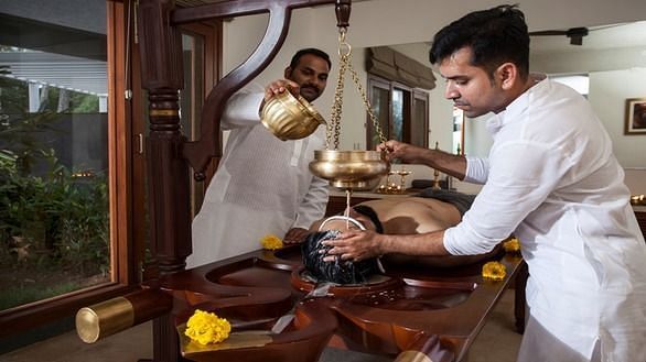 A therapist pouring warm herbal oil on a client’s back during an Ayurvedic treatment - Shreyas Retreat