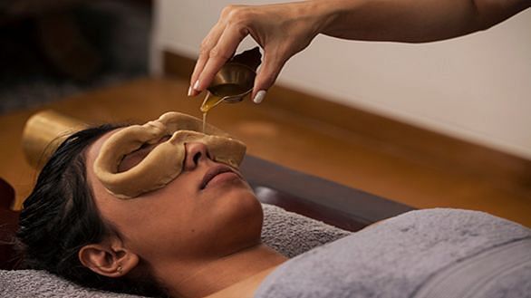A close-up of a person receiving a treatment on their face, wooden table - Shreyas Retreat