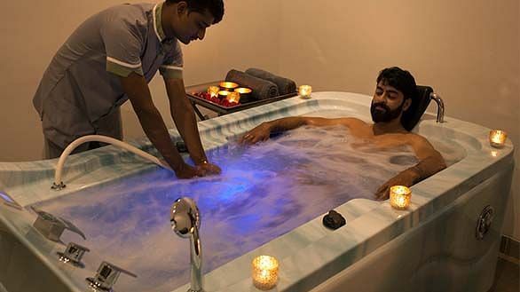 A person receiving a massage on a lit-up table, with another person standing - Shreyas Retreat