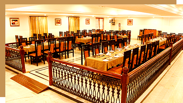 A spacious, well-lit Tycoon restaurant dining area at Jenneys Residency with rows of neatly arranged tables and chairs, set with tablecloths and place settings, surrounded by wooden railings