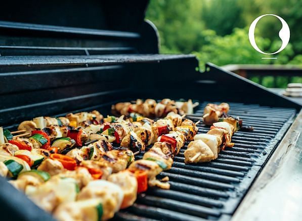 A close up shot of several skewers with seasoned vegetables kept over a barbecue grill.