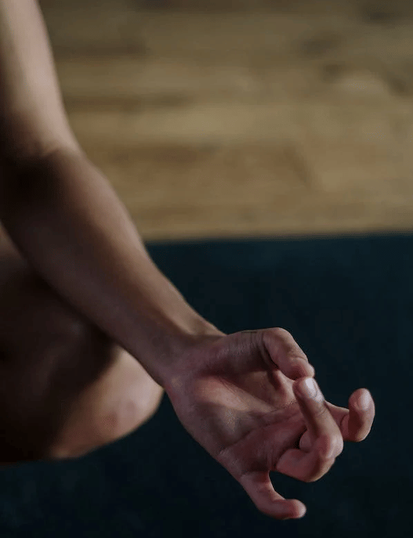 a person's hand in a yoga mudra, fingers gently touching, against a dark mat