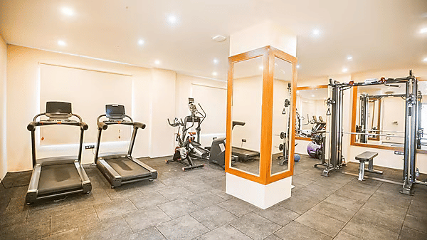 A brightly lit panorama of the gym featuring a pillar in the middle with full-length mirrors and a padded flooring throughout at Leroy Grand, Yeshwanthpur.