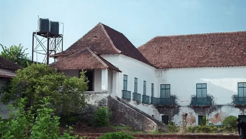 A heritage building with sloped tiled roofs, arched windows, and an external staircase surrounded by greenery.