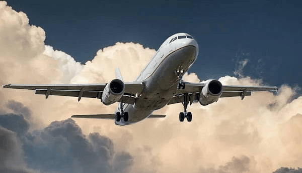 An airplane soaring through the sky with clouds in the background.