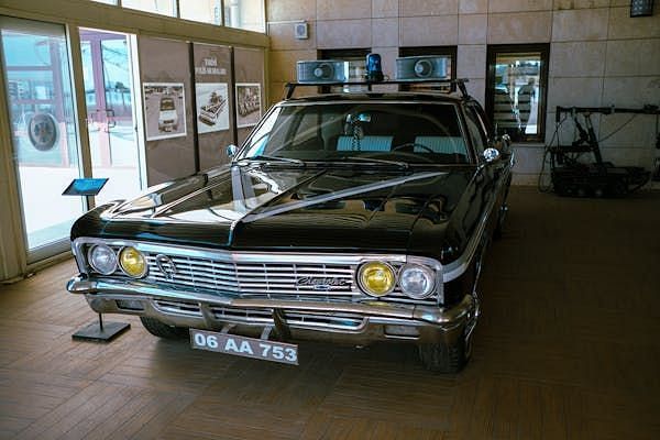 Classic black Chevrolet police car with roof lights displayed inside an automobile museum.