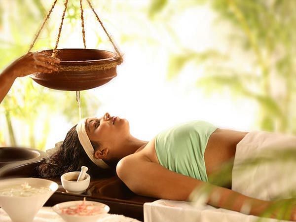 Woman receiving an Ayurvedic therapy with oil being gently poured on her forehead at a spa.
