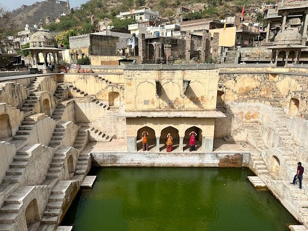 A stepped water reservoir descends to a pool, framed by architectural structures and people.