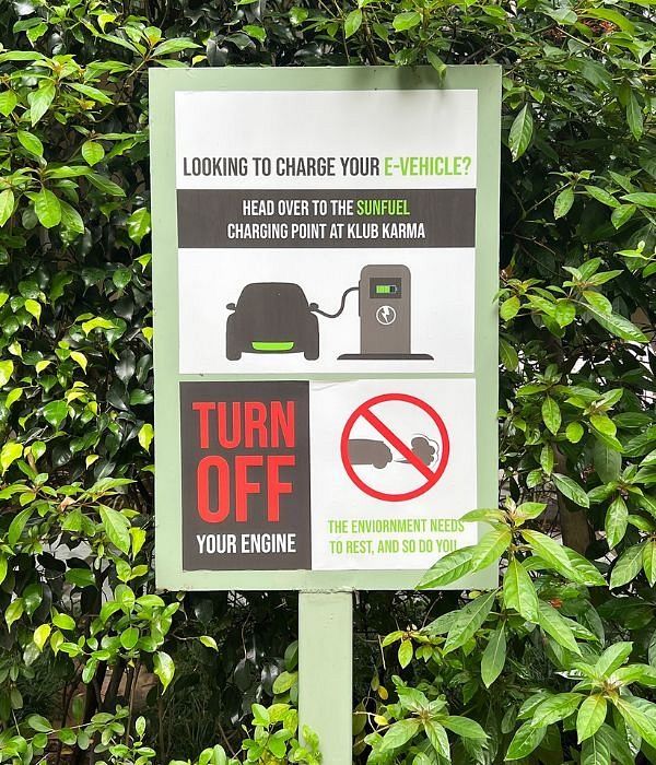 Sign instructing drivers to turn off engines and avoid honking, set against green foliage at Karma Chalets.