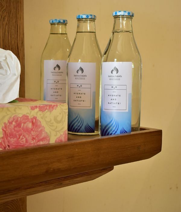 Shelf holding glass water bottles and boxed tissues near a wall with a wooden edge at Karma Chalets.