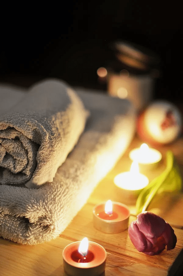 A warm and inviting spa setting with a fluffy towel, candles, and a fresh flower, creating a peaceful ambiance.