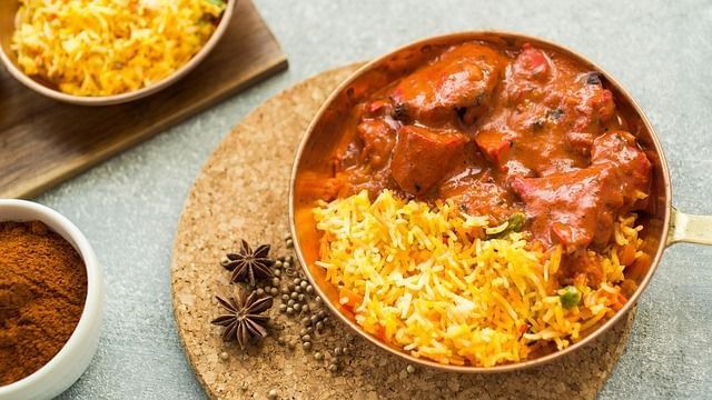 Chicken curry and saffron rice in a copper pot, garnished with spices.