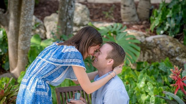 A woman in a blue and white dress leaning to kiss a man seated outdoors amid lush greenery at Casa Morada.
