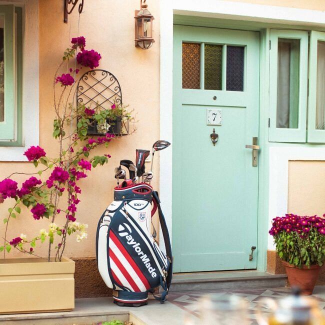 Entrance to a pastel coloured villa with a mint green door, potted flowers, and golf bags near the wall at Karma Chalets.