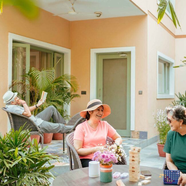 Three people sitting on a patio outside a peach coloured building, engaged in conversation at Karma Chalets.