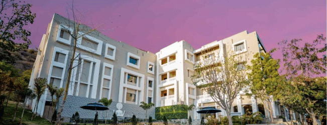 Facade of Essentia Luxury Resort and Spa, Udaipur with trees on the side.