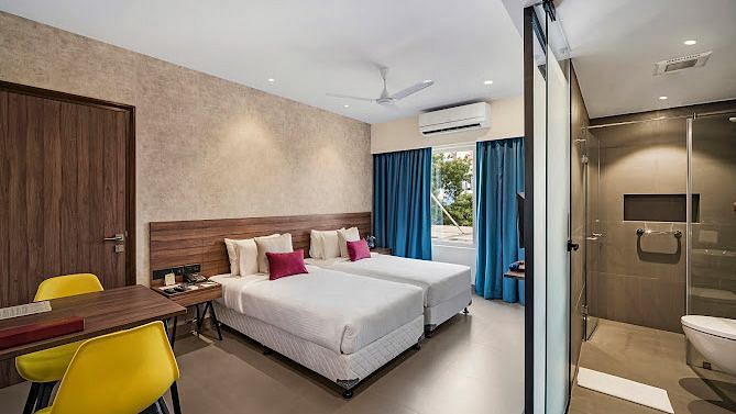 One of our rooms in thoothukudi with twin beds, a table with yellow chairs, and a modern shower area in front - Regency Tuticorin by GRT Hotels