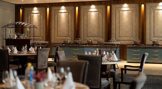 The inviting buffet area at Nirvana Luxury Hotel, Ludhiana, features arranged food stations and set dining tables with comfortable chairs in a softly lit ambience.