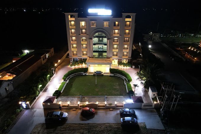 The exterior of a hotel building illuminated at night with a paved pathway and garden | Daksh The Madhuvan Suites