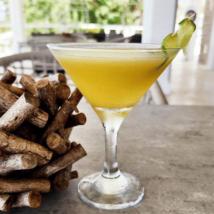 A yellow cocktail in a martini glass next to a stack of brown pastries or snacks.