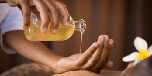 Hands pouring oil onto another person’s back with a flower on their ear