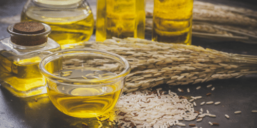Glass jars containing oil placed beside grains and natural materials on a flat surface