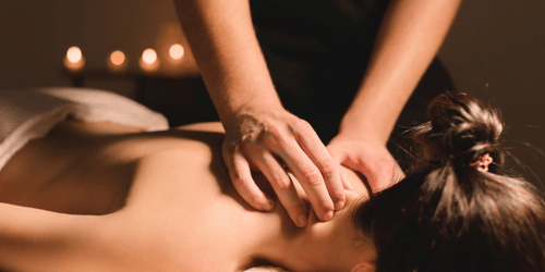 A person lying face down in a warmly lit environment and receiving massage on the back of their neck at YO1 Longevity & Health Resorts
